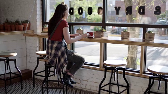WS。一个十几岁的女孩在市中心一家咖啡店的阳光窗边的座位上喝着拿铁。视频下载