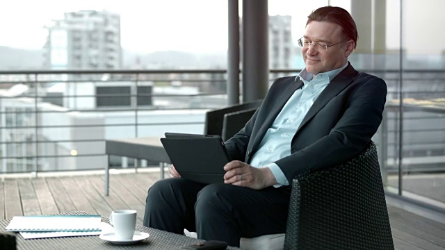 一名白人男子微笑着在城市的一个露台休息室里使用他的数字平板电脑视频素材