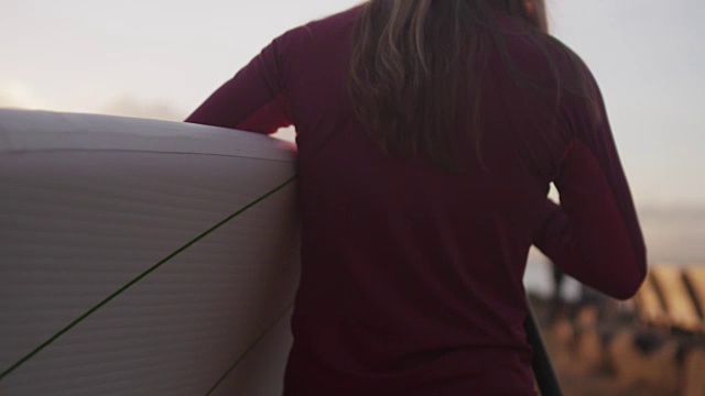 黎明时分，一个女人带着冲浪板走着，慢镜头视频下载