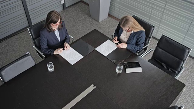 在会议室的桌子上方，两位女商人正在签署一份合同并握手视频素材