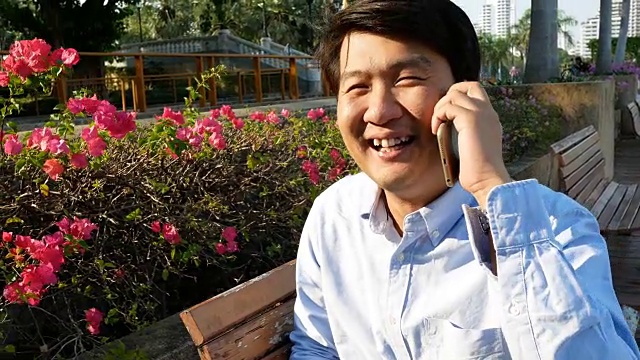 年轻的亚洲男人坐在外面用手机视频下载