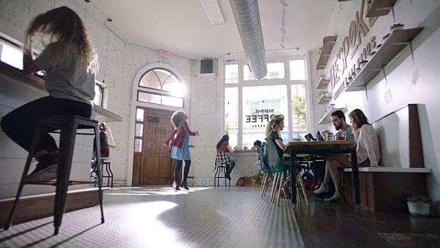 一名年轻女子戴着耳机，在市中心一家阳光明媚的咖啡馆里随着智能手机上的音乐跳舞，没人看。视频素材