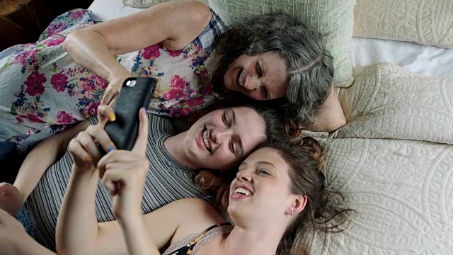 两姐妹看着手机和妈妈在床上笑。视频下载