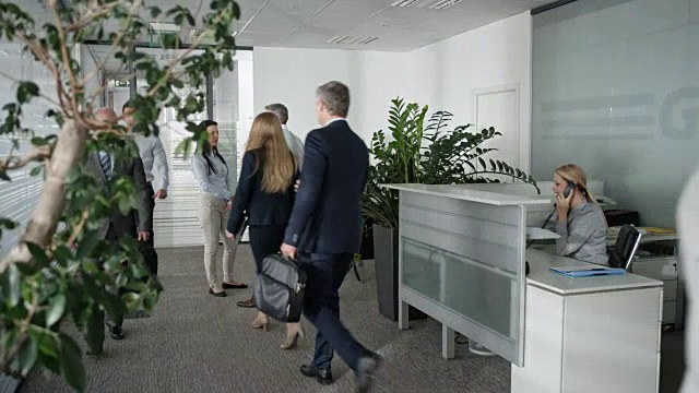 一个微笑的商人结束电话，微笑着走进办公室走廊的镜头视频素材
