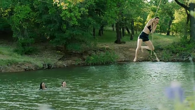 朋友们看着女孩在秋千上荡来荡去，然后跳进河里。视频素材
