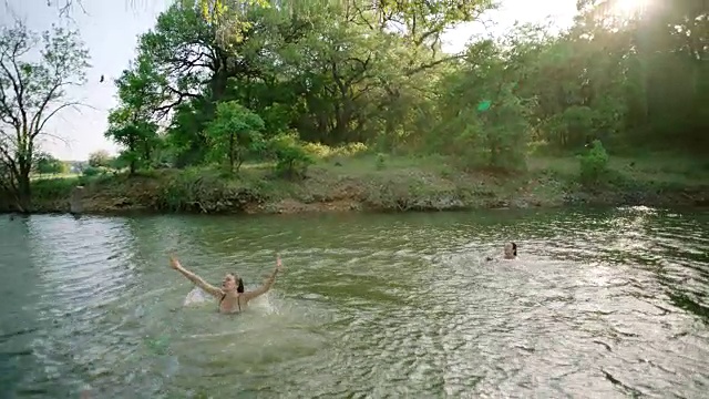 女孩带着绳子在河上荡秋千，在朋友们的鼓励下跳入水中。视频素材