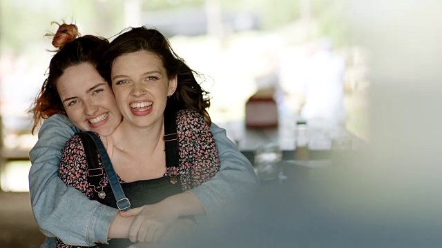 两姐妹在户外野餐亭对着镜头拥抱微笑。视频素材