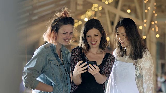 三个女孩摆姿势自拍，亲吻脸，看智能手机，笑。视频素材