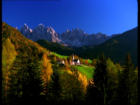 一座乡村教堂坐落在白雪覆盖的阿尔卑斯山下的绿色山谷中。视频下载