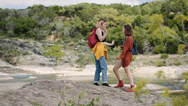 在国家公园徒步旅行的两姐妹在俯瞰河流的山顶上跳舞。视频素材
