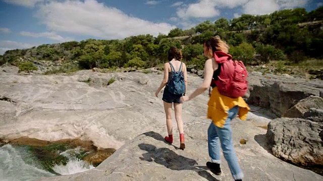 在佩德奈尔斯瀑布州立公园，两个背着背包徒步旅行的女孩停下来勘察岩石地形和咆哮的河流。视频素材