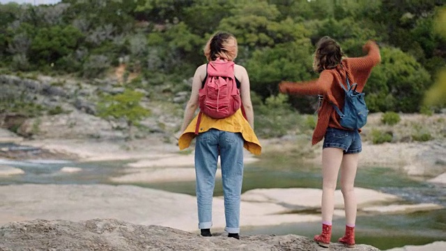在佩德奈尔斯瀑布州立公园徒步旅行时，两个女孩停下来，向空中举手并在河边跳舞。视频素材
