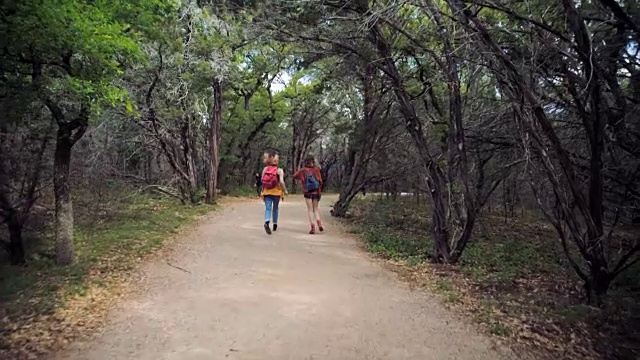 两个姐妹跑和跳跃下绿色森林小径。视频素材