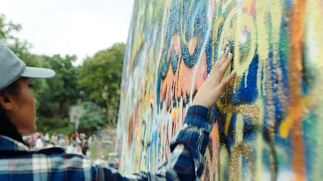 小女孩手扶着彩色涂鸦墙奔跑。视频下载