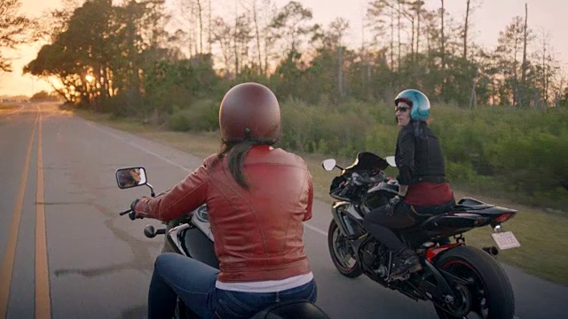 两名女子骑着摩托车，在日落时分互相嘲笑。视频素材