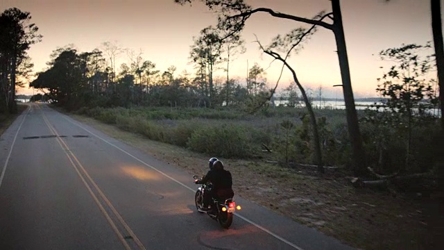 日落时分，一对夫妇骑着摩托车沿着海岸公路行驶。视频下载