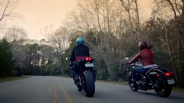两个女人骑着摩托车在空旷的森林路上行驶。视频素材