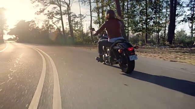 一名年轻女子在空旷的沿海公路上驾驶摩托车驶向阳光。视频下载