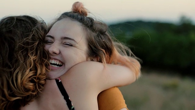 两姐妹在山腰的绿色田野里拥抱。视频素材