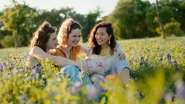 三个女孩坐在花丛中大笑。视频素材