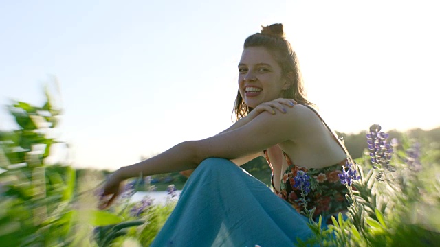 女孩SLO MO坐在鲜花的田野里，对着镜头笑。视频素材