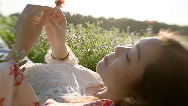 抱着花躺在绿色的田野里的女孩转身对着镜头微笑。视频下载