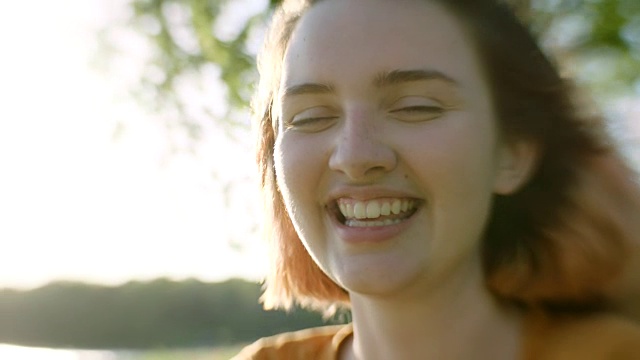 女孩坐在阳光灿烂的草地上的树下，对着镜头微笑。视频素材