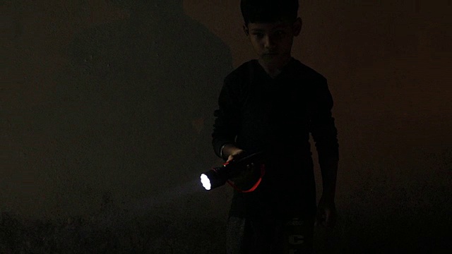 一个小男孩拿着电筒在黑暗中寻找。视频下载