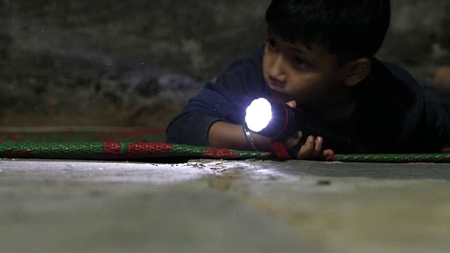 一个小男孩拿着电筒在黑暗中寻找。视频下载
