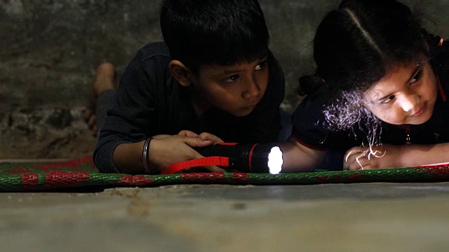 一个小男孩和一个小女孩拿着手电筒在黑暗中寻找。视频下载