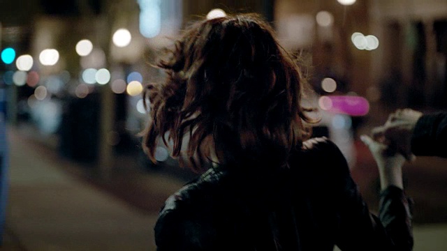 一名年轻男子晚上在城市的人行道上和女友转圈。视频素材