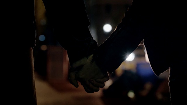 年轻夫妇手牵着手走过夜晚的城市。视频素材