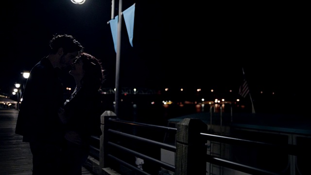 一对年轻夫妇在河边木板路的路灯下拥抱。视频素材