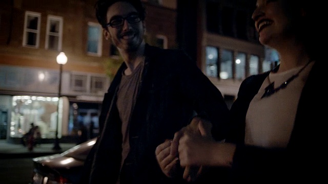 一对年轻夫妇手牵手走在夜晚的城市人行道上。视频素材