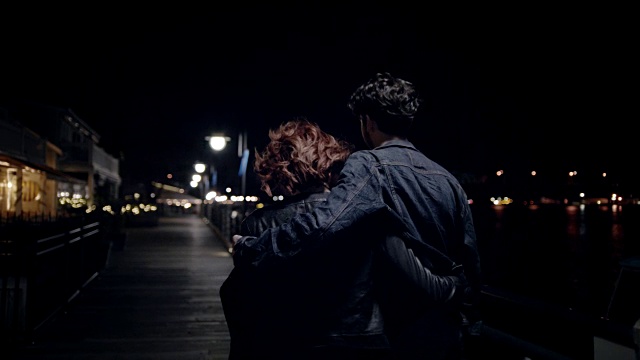一对年轻夫妇在夜晚漫步在海滨木板路上。视频素材
