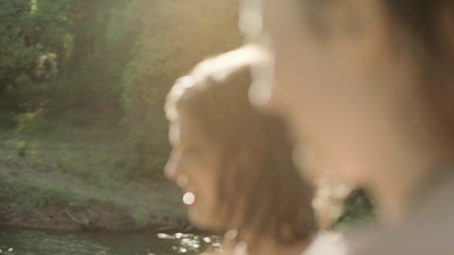 阳光明媚的一天，女孩在河边和朋友转过身笑。视频素材