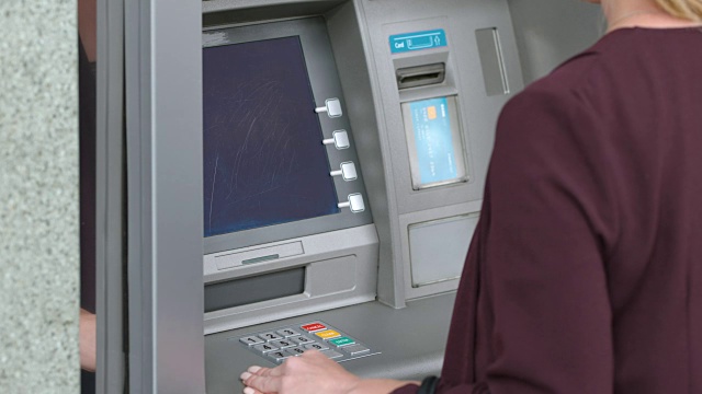 一名女子将一张银行卡插入ATM插槽，并在键盘上输入她的密码视频素材