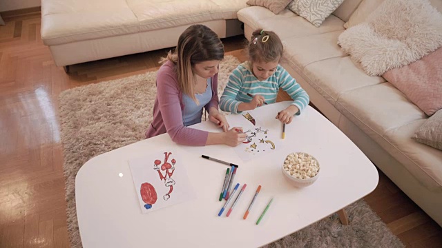 快乐的小女孩和妈妈在家里的一张纸上涂色。视频素材