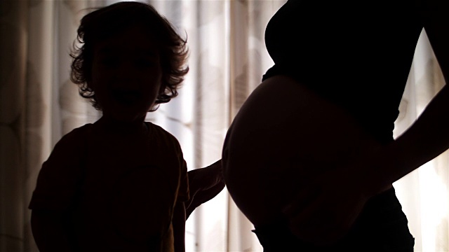 慢动作:蹒跚学步的儿子亲吻怀孕的肚子视频素材