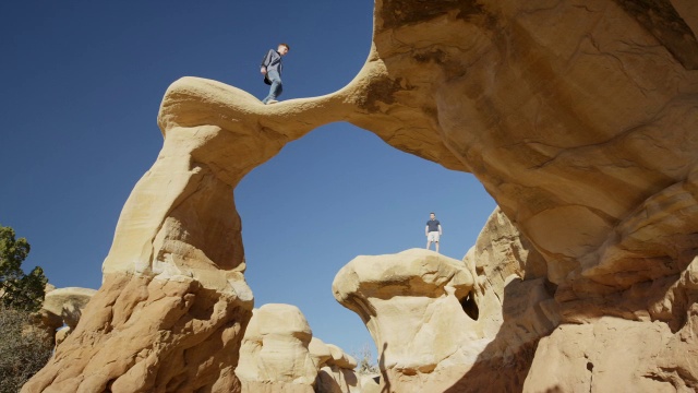 宽平移低角度拍摄的人行走在拱形岩层/埃斯卡兰特，犹他州，美国视频下载