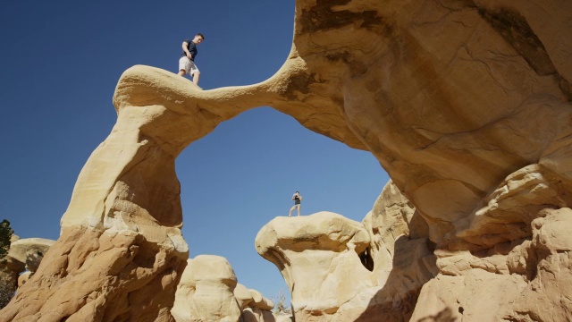 宽平移低角度拍摄的人行走在拱形岩层/埃斯卡兰特，犹他州，美国视频下载