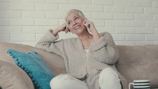 快乐成熟的女人，一边在沙发上放松，一边和某人通过手机聊天。视频素材