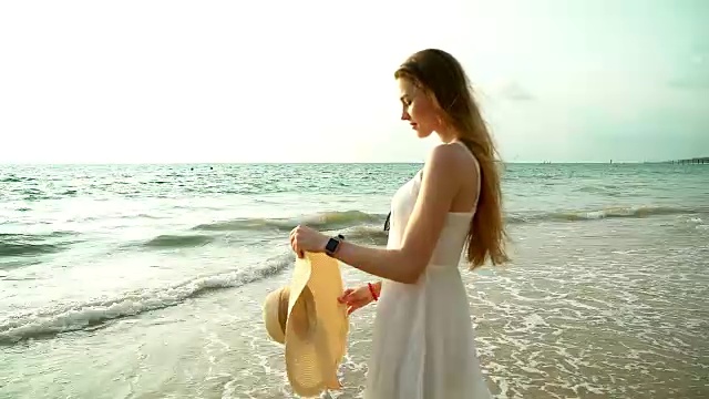 海滩上快乐微笑的女人的肖像。微笑性感的金发女郎在美丽的野生海滩摆姿势。美丽的女孩在不经意的看着夕阳。视频素材