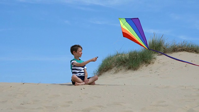 一个小男孩看着他的风筝在海滩上飞。视频素材