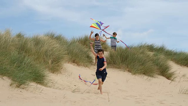 三个孩子在沙丘上奔跑，在海滩上放风筝。视频素材