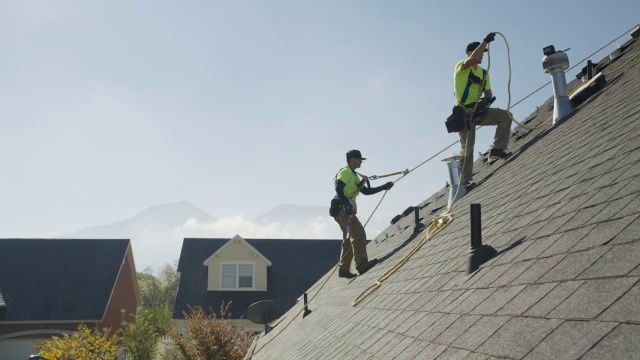 宽平移低角度拍摄工人在屋顶上钻孔/ Mapleton，犹他州，美国视频素材