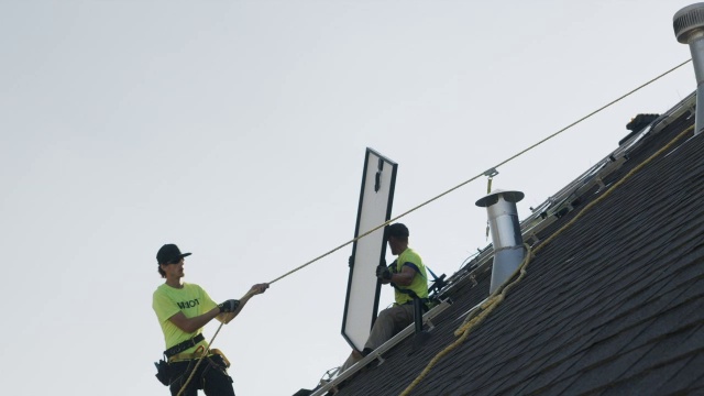宽平移低角度拍摄工人在屋顶上携带太阳能电池板/ Mapleton，犹他州，美国视频素材