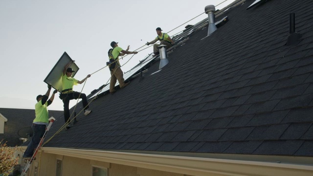 宽平移低角度拍摄工人在屋顶上携带太阳能电池板/ Mapleton，犹他州，美国视频素材