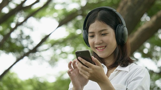 亚洲年轻女性听音乐与无线耳机在秋季公园-播客视频下载