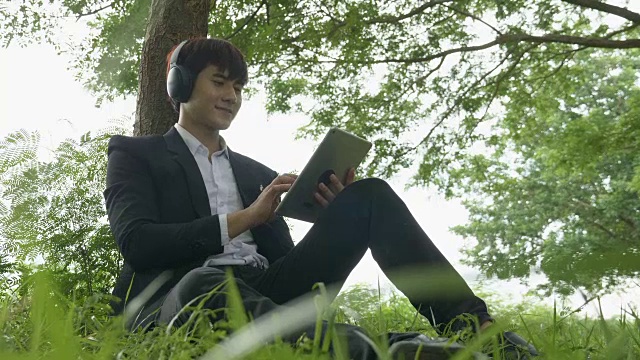 亚洲年轻男性在秋季公园用无线耳机听音乐-播客视频下载